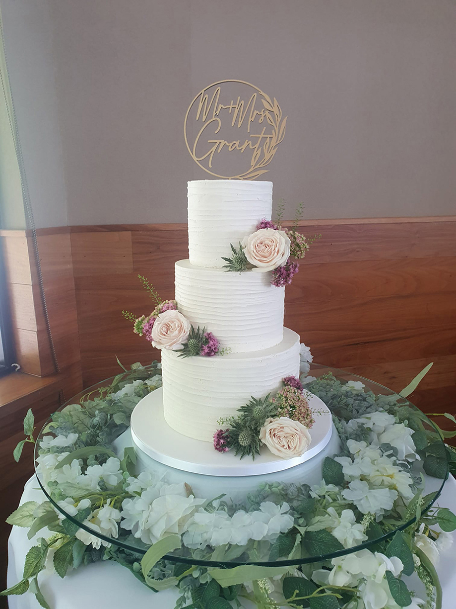 White three-tier cake with light pink roses and gold circular cake topper